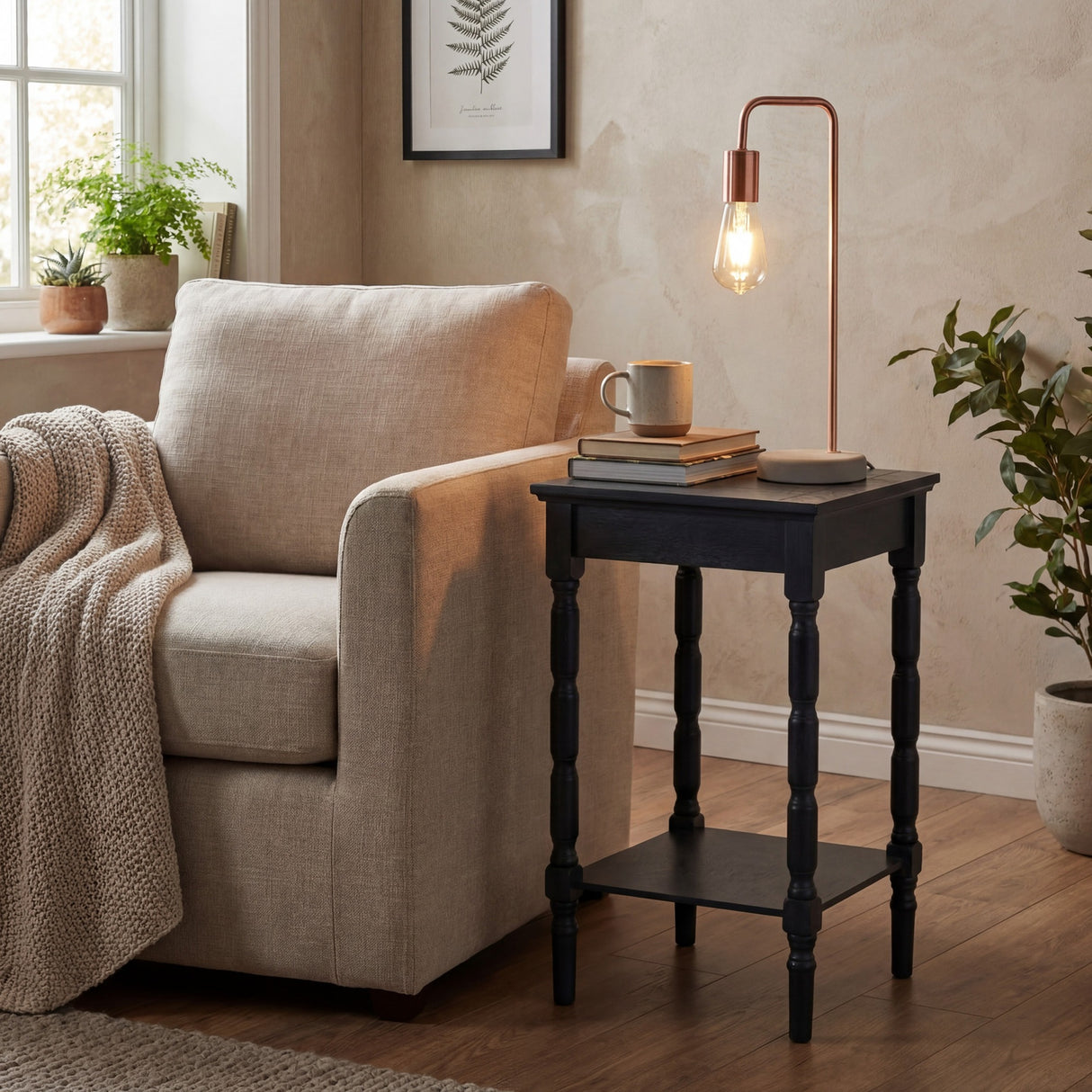 Hill Interiors copper industrial table lamp with exposed bulb and stone base on a black turned-leg side table beside a beige armchair in a living room.