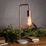 Hill Interiors copper industrial table lamp with an upright metal frame, exposed Edison bulb and round stone base, styled with books and foliage.