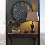 Hill Interiors large round wall clock with black face, brass numerals and frame, displayed above a wooden console table with lamp and florals.