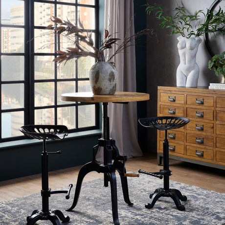 Hill Interiors adjustable height bar bistro table with round wood top and black metal crank base, styled with tractor stools by an industrial window.