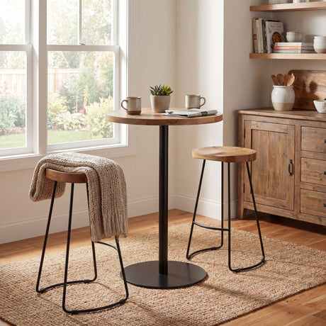 Hill Interiors hardwood bar table with round brown timber top and black metal pedestal, styled with two wooden stools in a sunlit kitchen corner.