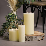Hill Interiors set of three LED cream wax pillar candles grouped on a wood slice beside eucalyptus, pampas grass in a glass vase and a black chair.