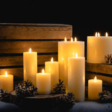 Hill Interiors LED cream wax pillar candles in assorted heights, grouped with pinecones against a rustic wooden crate for a warm, flickering display.