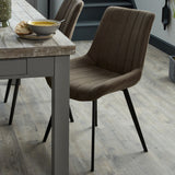 Hill Interiors Draxinby brown faux-leather dining chair with contoured stitched back and slim black tapered legs, set beside a rustic wooden dining table.
