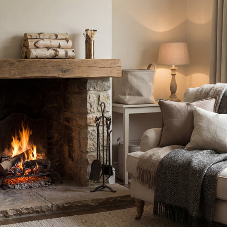 Hill Interiors antique bronze matchstick holder filled with long matches on a rustic wooden mantel beside stacked birch logs above a lit stone fireplace.