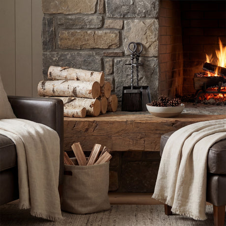 Hill Interiors hearth tidy companion set with hand-turned loop handle and shovel beside stacked birch logs on a rustic wooden mantel by a lit fireplace.