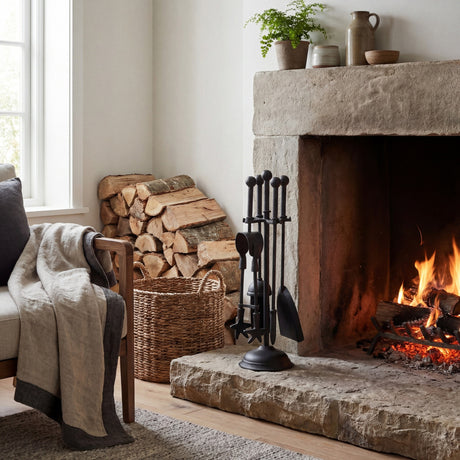 Hill Interiors Ball Topped Companion Set in matt black metal beside a stone fireplace, holding poker, brush, shovel and tongs on a ball-finial stand.