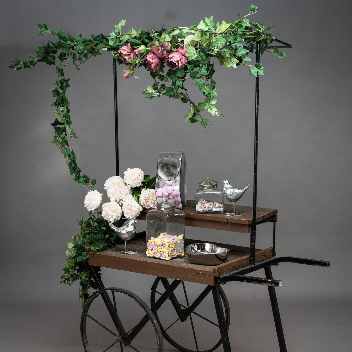 Hill Interiors 200cm faux ivy garland draped over a wooden cart with pink and cream faux roses, glass sweet jars and silver bird ornaments.