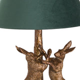 Close-up of Hill Interiors Antique Gold Hares table lamp base, showing two sculpted resin hares in aged gold finish beneath a green velvet shade.