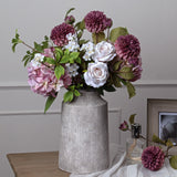 Hill Interiors urn-shaped stone-effect ceramic vase in beige, holding pink roses, mauve dahlias and hydrangeas on a wooden console against a pale wall.