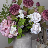 Hill Interiors urn-shaped stone-effect ceramic vase in beige, holding an arrangement of mauve dahlias, blush roses, pink hydrangea and white blossom.