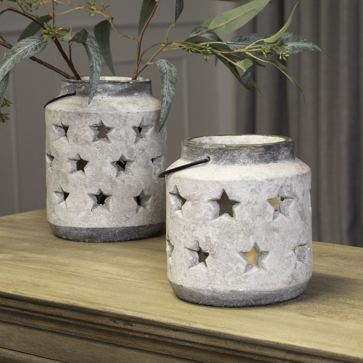 Hill Interiors Large Stone Star Lantern ceramic candle holders in beige with pierced star cut-outs and wire handles, styled with foliage on a wooden sideboard.