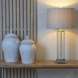 Two Hill Interiors Stone Ginger Jar ceramic vases in beige with domed lids on a wooden console beside a fluted glass table lamp with grey shade.