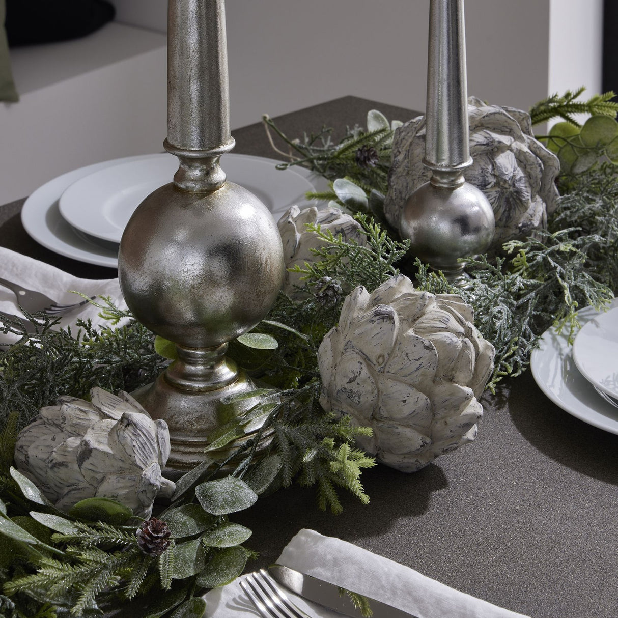 Hill Interiors white resin artichoke ornaments styled on a festive table with silver candlesticks, frosted greenery and white plates.