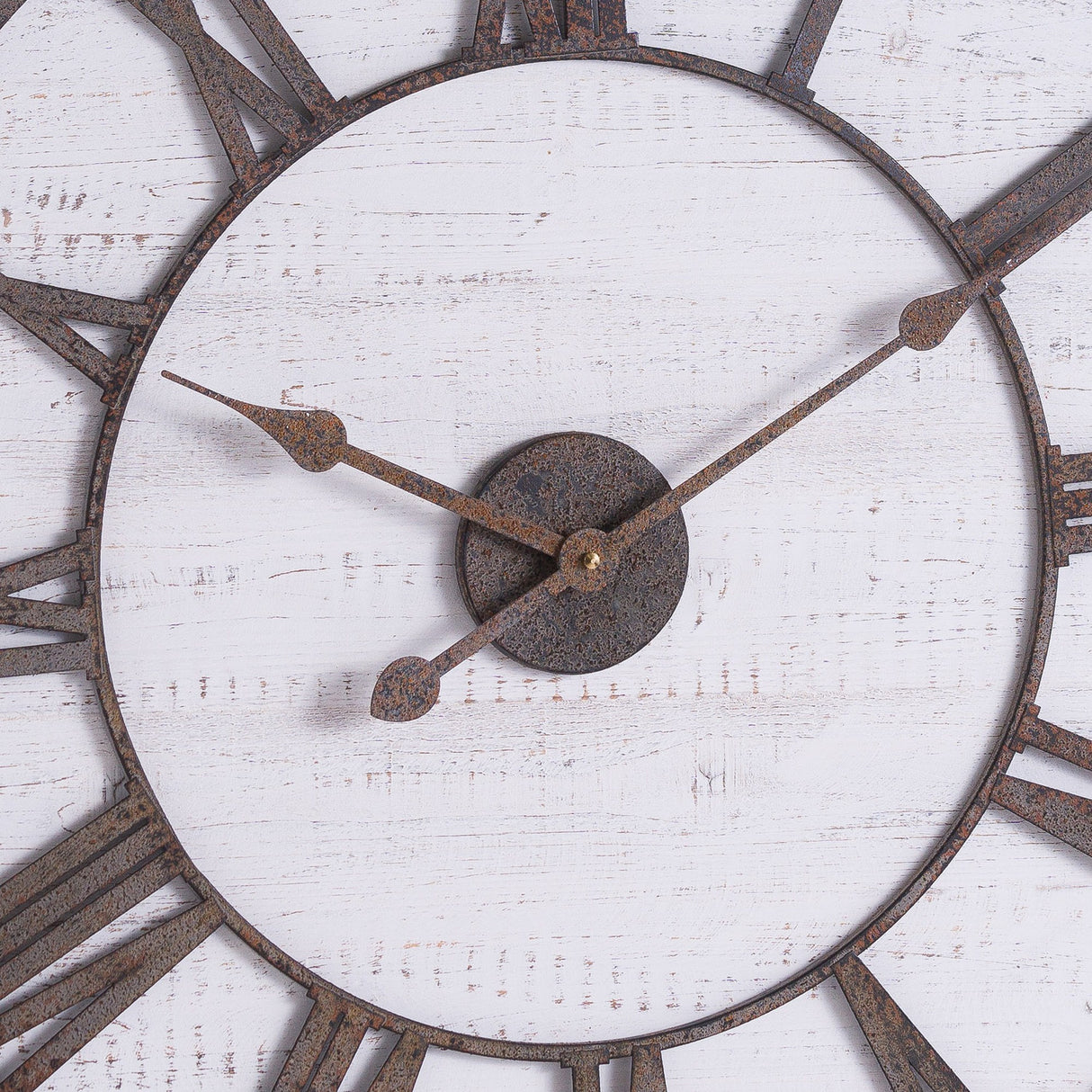 Close-up of Hill Interiors rustic wooden wall clock showing aged brass Roman numerals and hands on a whitewashed timber face with visible grain.