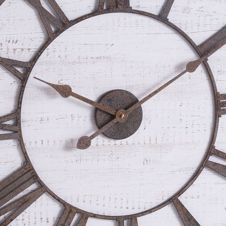 Close-up of Hill Interiors rustic wooden wall clock showing aged brass Roman numerals and hands on a whitewashed timber face with visible grain.