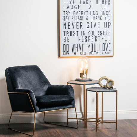 Hill Interiors Set of 2 Gold and Black Marble-Effect Side Tables styled beside a navy velvet armchair with a glass dome lamp and framed wall art.