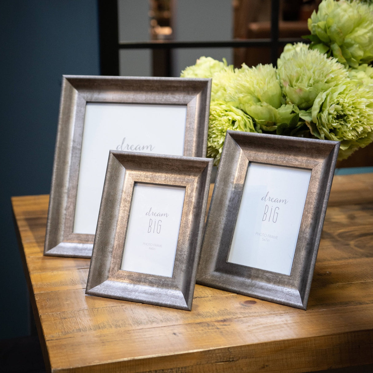 Three Hill Interiors Convex Matt Silver photo frames in varying sizes displayed on a wooden table beside green hydrangeas, holding 5x7in and 4x6in prints.