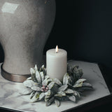 Hill Interiors Natural Glow LED wax pillar candle in beige, 15cm, lit and set within a frosted foliage ring beside a crackle-glaze lamp base.