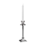Hill Interiors Natural Glow LED dinner candle in beige plastic, shown lit in a tall silver candlestick with square base on a white background.
