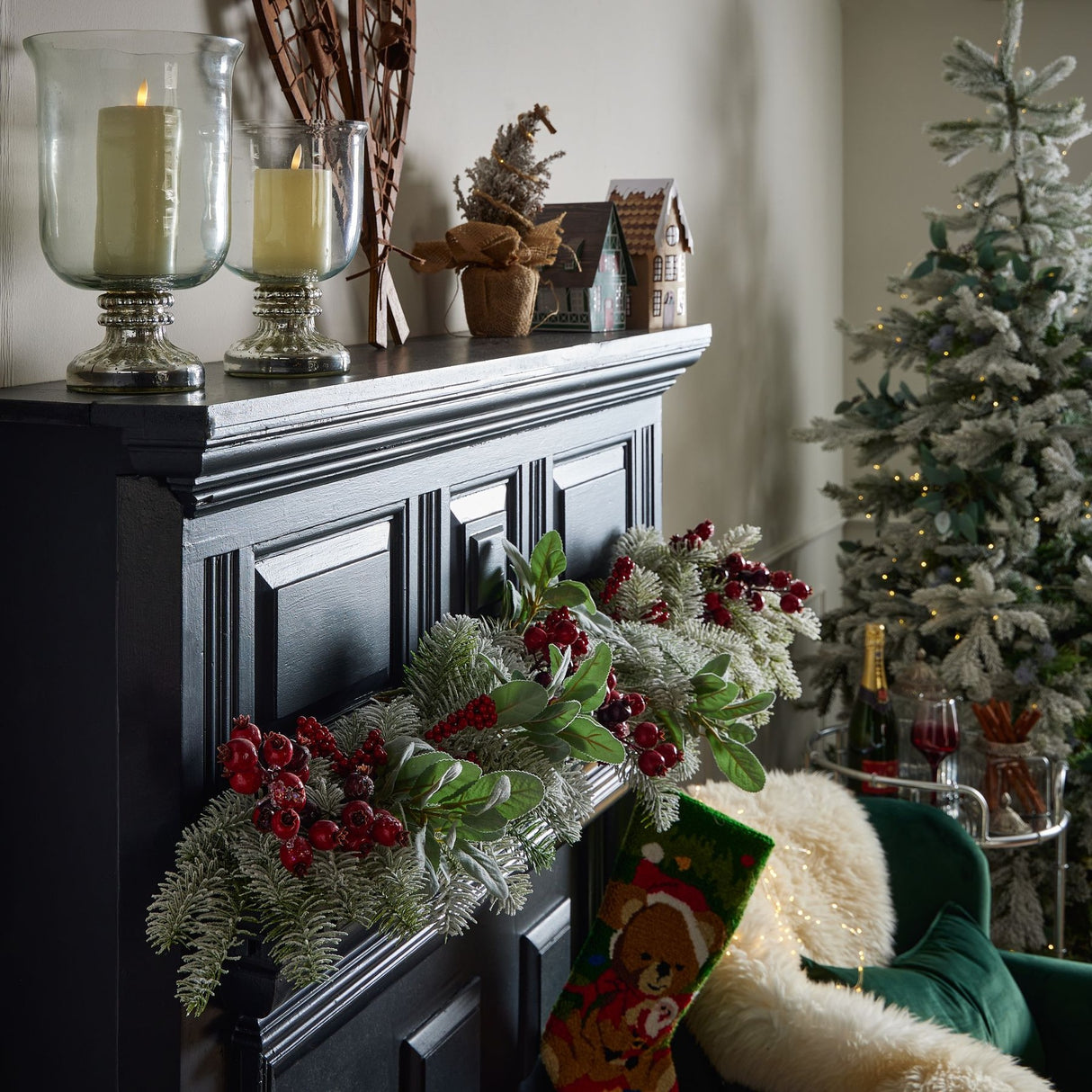 Hill Interiors Fat Red Berry faux stem pick draped along a black panelled mantelpiece with flocked pine, beside candles and a Christmas tree.