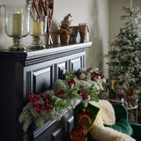 Hill Interiors Fat Red Berry faux stem pick draped along a black panelled mantelpiece with flocked pine, beside candles and a Christmas tree.