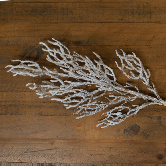Hill Interiors Snow Covered Branch in white plastic with frosted snow-effect finish, laid across a rustic wooden plank surface.