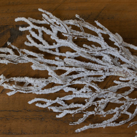 Hill Interiors Snow Covered Branch in white plastic with slender twigs dusted in snow effect finish, laid on a warm wooden surface.