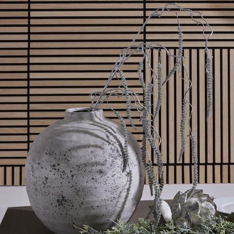 Hill Interiors Festive Faux Amaranthus Stem 130cm in silver, trailing from a distressed grey round vase against a slatted wood panel backdrop.