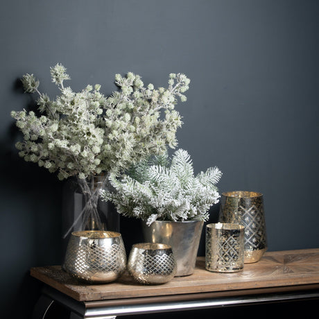 Hill Interiors Festive Snow Branch in white displayed in a glass vase with a frosted pine stem and mercury glass tealight holders on a wooden console.