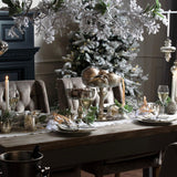 Hill Interiors Snowy Faux Garland of frosted pine foliage draped above a festive dining table set with candles, glassware and a flocked Christmas tree.
