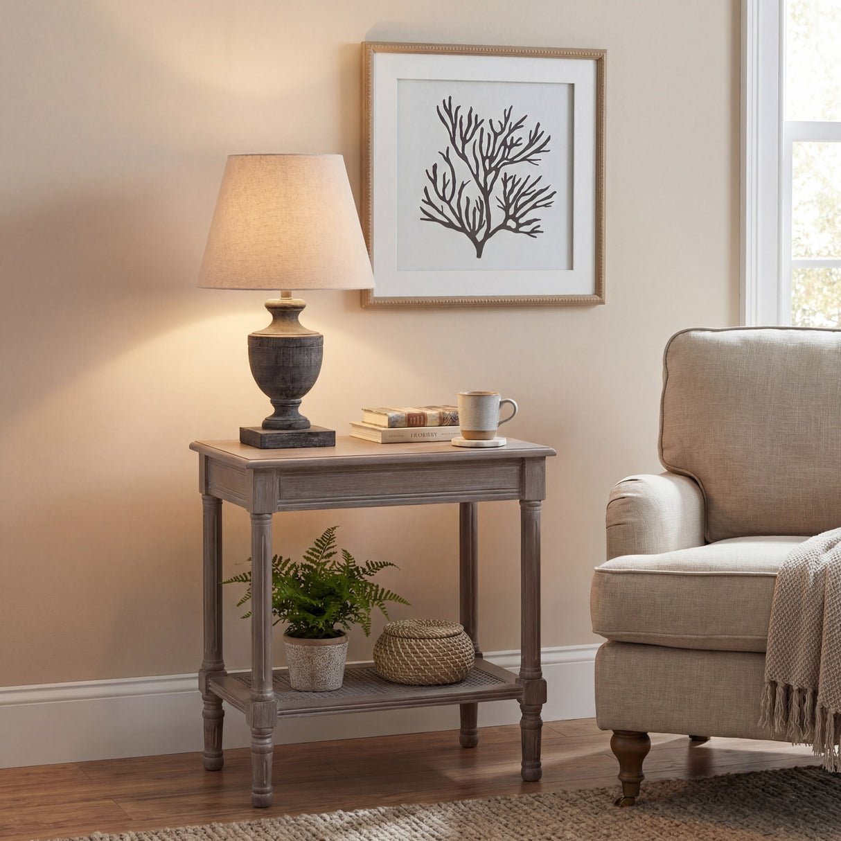 Hill Interiors Ondelle Urn Wooden Table Lamp in brown with tapered cream shade, lit on a grey side table beside an armchair and framed coral print.