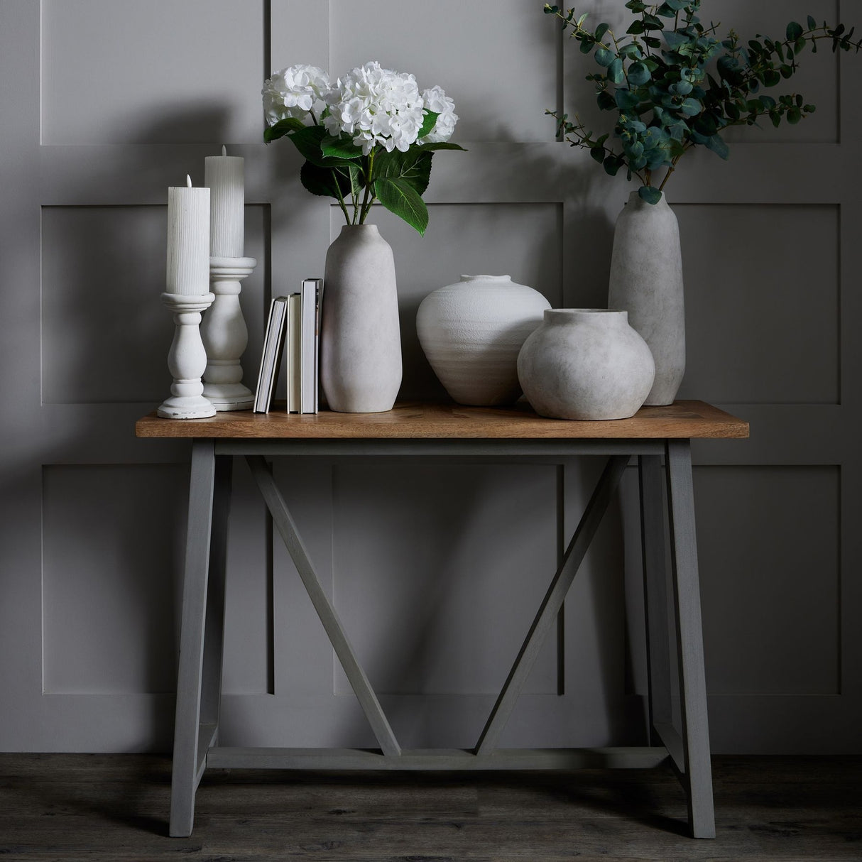 Hill Interiors Large Tall Ceramic Vase in beige with white hydrangeas, styled on a wooden console with candles, books and grouped vases.