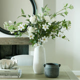 Hill Interiors Large Tall Ceramic Vase in beige holding white flowers and greenery on a wooden console beside a round black mirror and dark handled pot.