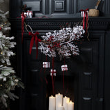 Hill Interiors Rocky the Robin metal ornament in brown perched on a black mantel above a festive display of white gifts, red ribbons and snowy branches.