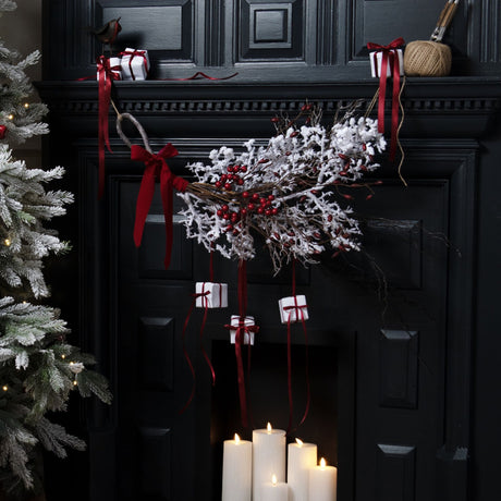 Hill Interiors Rocky the Robin metal ornament in brown perched on a black mantel above a festive display of white gifts, red ribbons and snowy branches.
