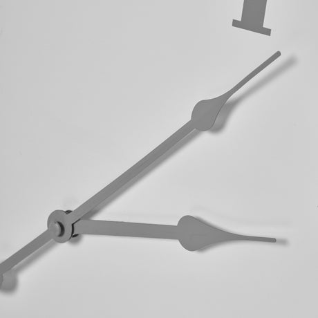 Close-up of Hill Interiors Round Metal Wall Clock in white, showing slim tapered grey hands at the central spindle and part of a numeral on the pale dial.
