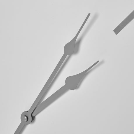 Close-up of Hill Interiors Round Metal Wall Clock in white, showing slender grey hour and minute hands meeting at the central spindle with a numeral edge.