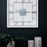 Hill Interiors White Square Large Wall Clock with slim metal frame and grey Roman numerals, mounted on a dark wall above eucalyptus and lanterns.