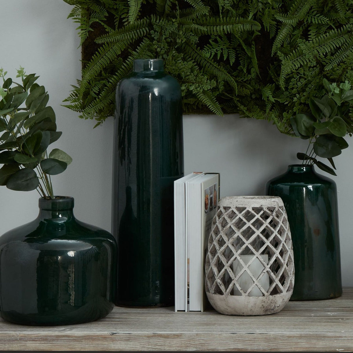 Hill Interiors Emerald Glazed Ceramic Eve Vase grouped with a taller green bottle vase, books and a stone lattice lantern beneath ferns.