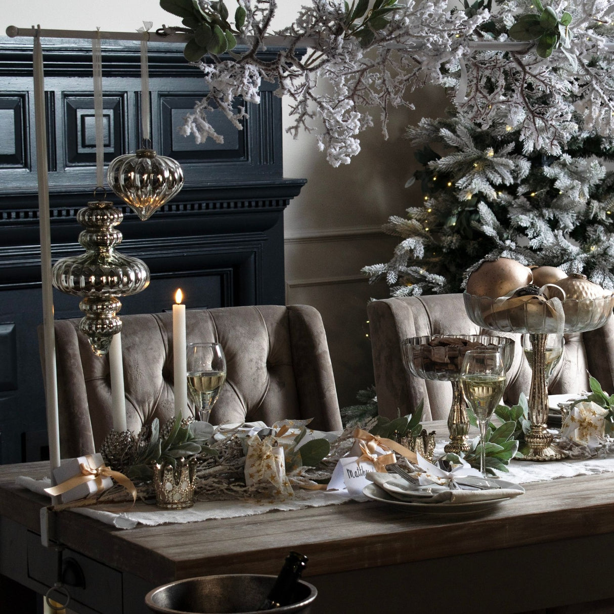 Hill Interiors large antique silver glass bauble hung above a Christmas table setting with candles, wine glasses and a flocked tree.