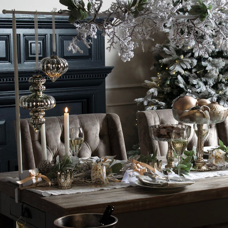 Hill Interiors large antique silver glass bauble hung above a Christmas table setting with candles, wine glasses and a flocked tree.