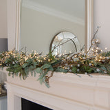 Hill Interiors warm white LED cluster string lights draped along a cream mantelpiece with foliage, pussy willow stems, and a framed mirror above.