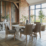 Hill Interiors matt white ceramic vase with foliage stems on a console beside a rustic wood-clad wall in a brick-walled dining room.
