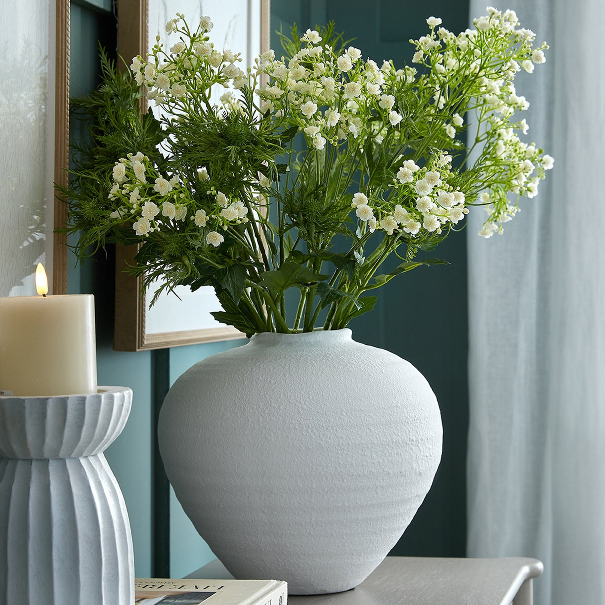 Hill Interiors Large Matt White Ceramic Vase with rounded body holding white gypsophila stems, styled on a console beside a candle and framed mirror.