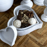Hill Interiors matt white ceramic heart-shaped bowls styled with pine cones, woven balls and dried botanicals on a parquet wood floor.