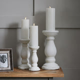 Hill Interiors matt white ceramic candle holders in three heights with lit pillar candles, arranged on a wooden console beside a framed print.