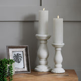 Two Hill Interiors matt white ceramic candle holders with lit pillar candles on a wooden console beside a framed print and trailing plant.