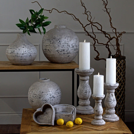 Hill Interiors stone-effect beige ceramic candle holders in three heights with lit white pillar candles, styled with textured vases, heart dishes and lemons.