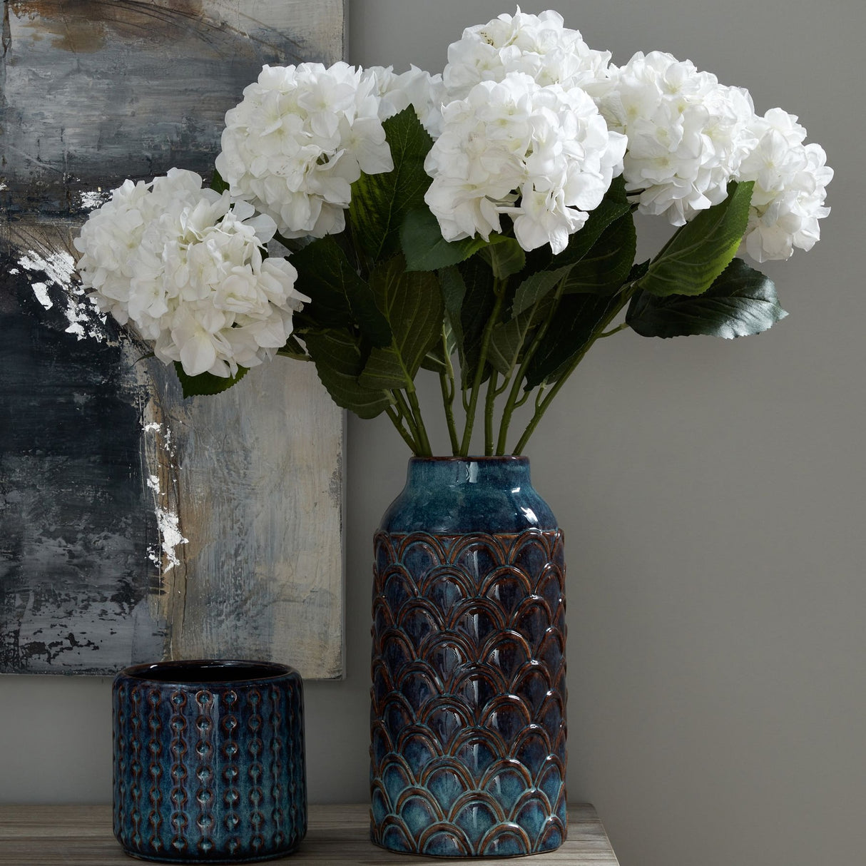 Hill Interiors Ceramic Indoor Planter in blue with scalloped glazed pattern, holding white hydrangeas beside a smaller textured blue pot on a sideboard.